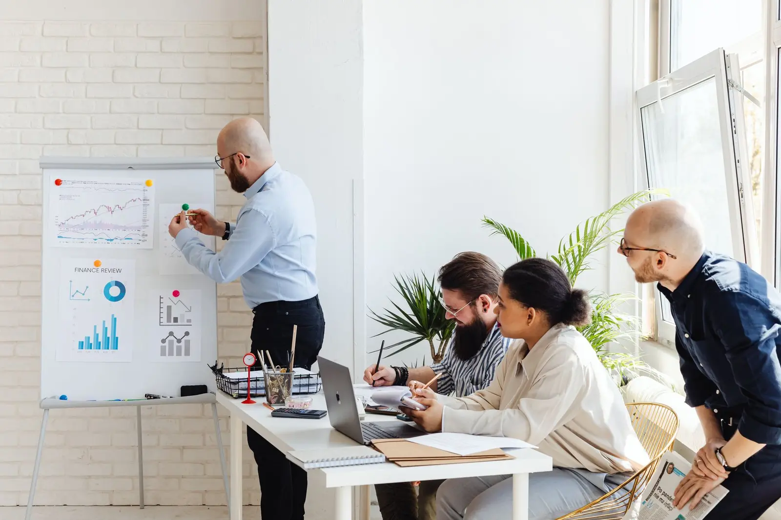 Team reviewing charts and data trends at a whiteboard in a bright room.