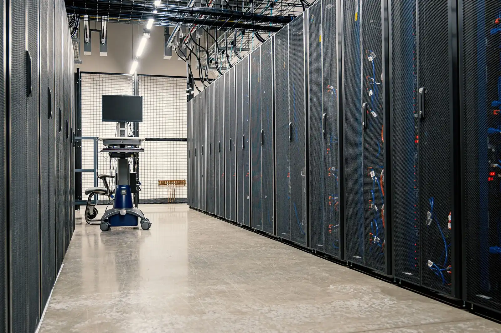 Data center aisle lined with server cabinets under lit ceiling tracks.