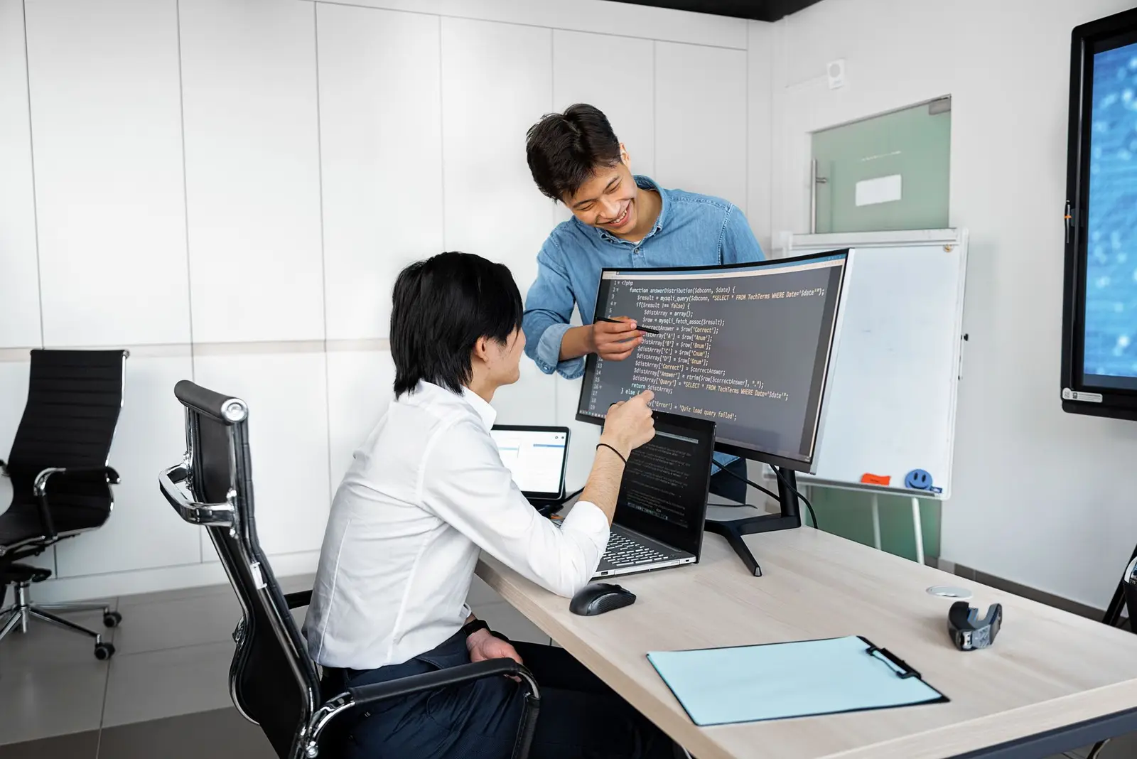 Two engineers reviewing code together on a monitor in a bright office.